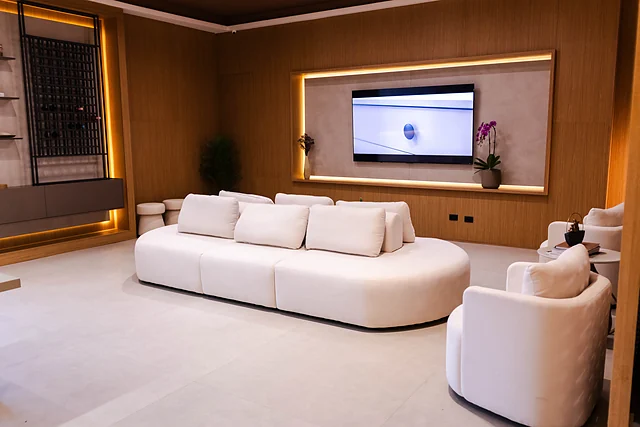 Sala com sofá curvo branco, poltronas e painel de TV em madeira com iluminação embutida